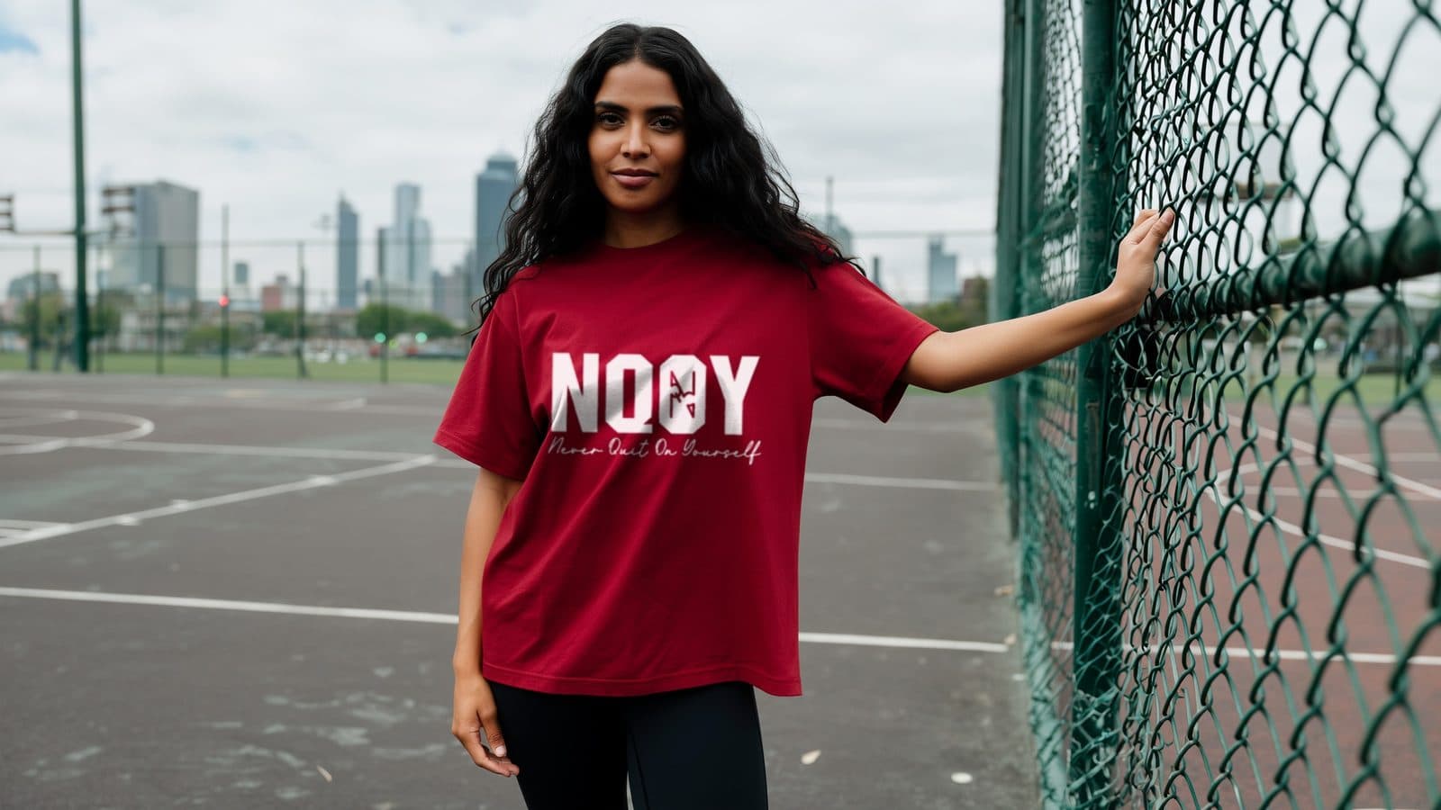 A woman wearing an NQOY cardinal tee on an outdoor city basketball court