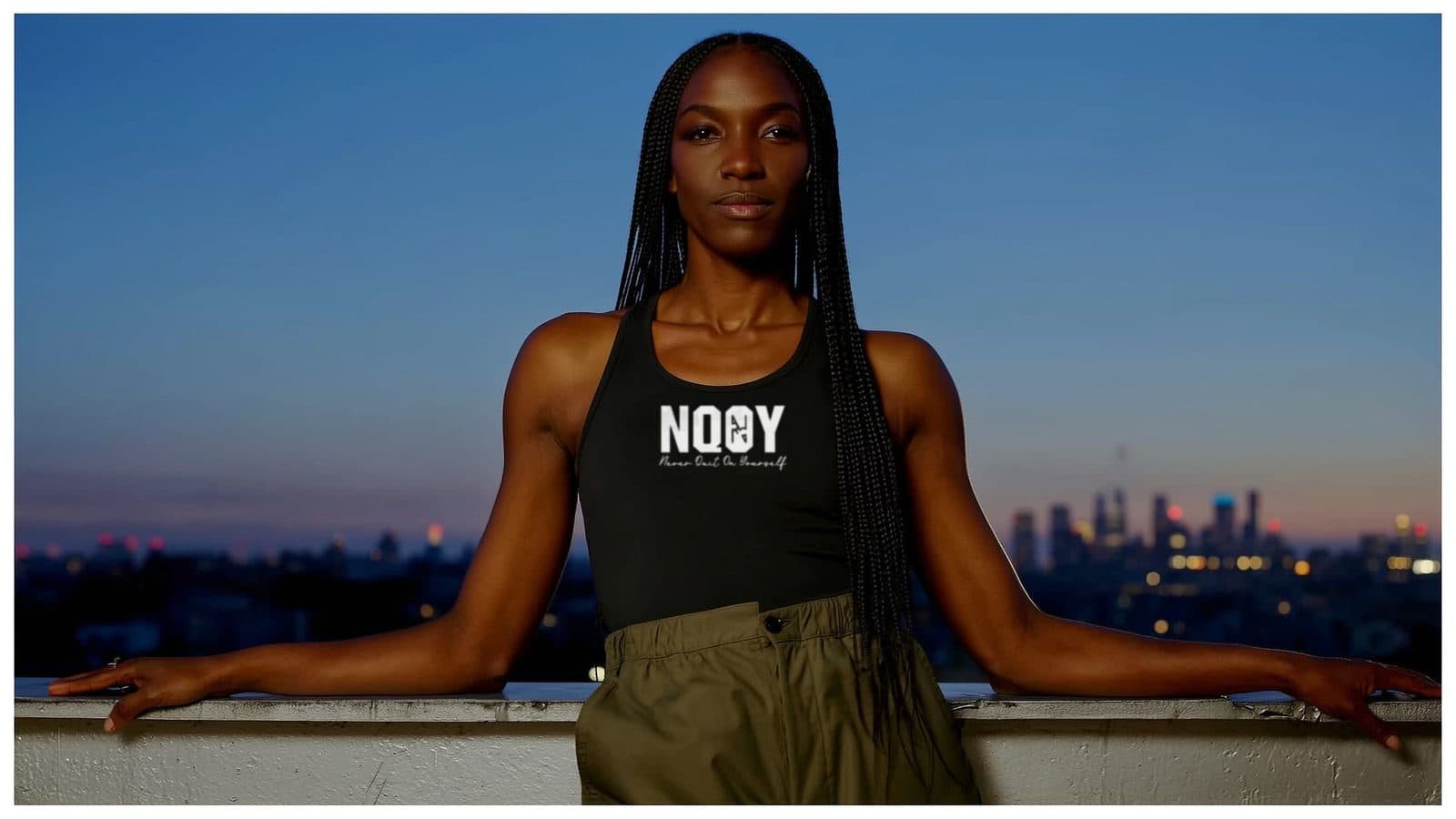 A woman in an NQOY tank on a city rooftop at dusk